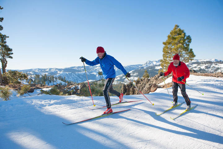 Senior X-C skiers gliding along with Royal Gorge behind their right shoulders. Credit: Snow Bowl/Royal Gorge